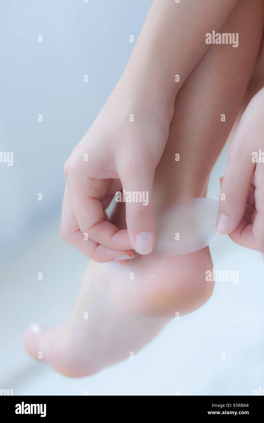 Woman putting a synthetic skin bandage on her heel. Stock Photo