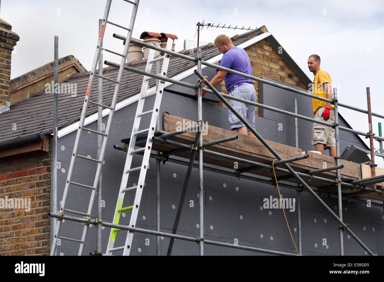 Builders attaching / fitting rigid foam wall insulation sheets / panels / boards to the gable end of Victorian terraced house UK Stock Photo