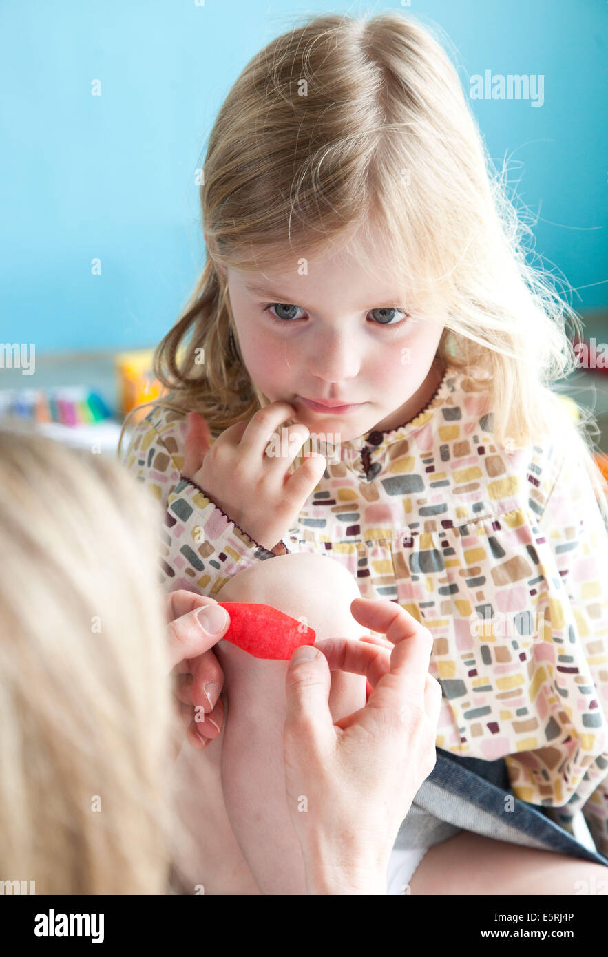 Mother applying band-aid on wounded knee of a girl. Stock Photo