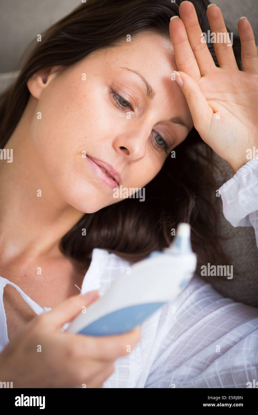 Woman taking her temperature with a digital tympanic thermometer. Stock Photo