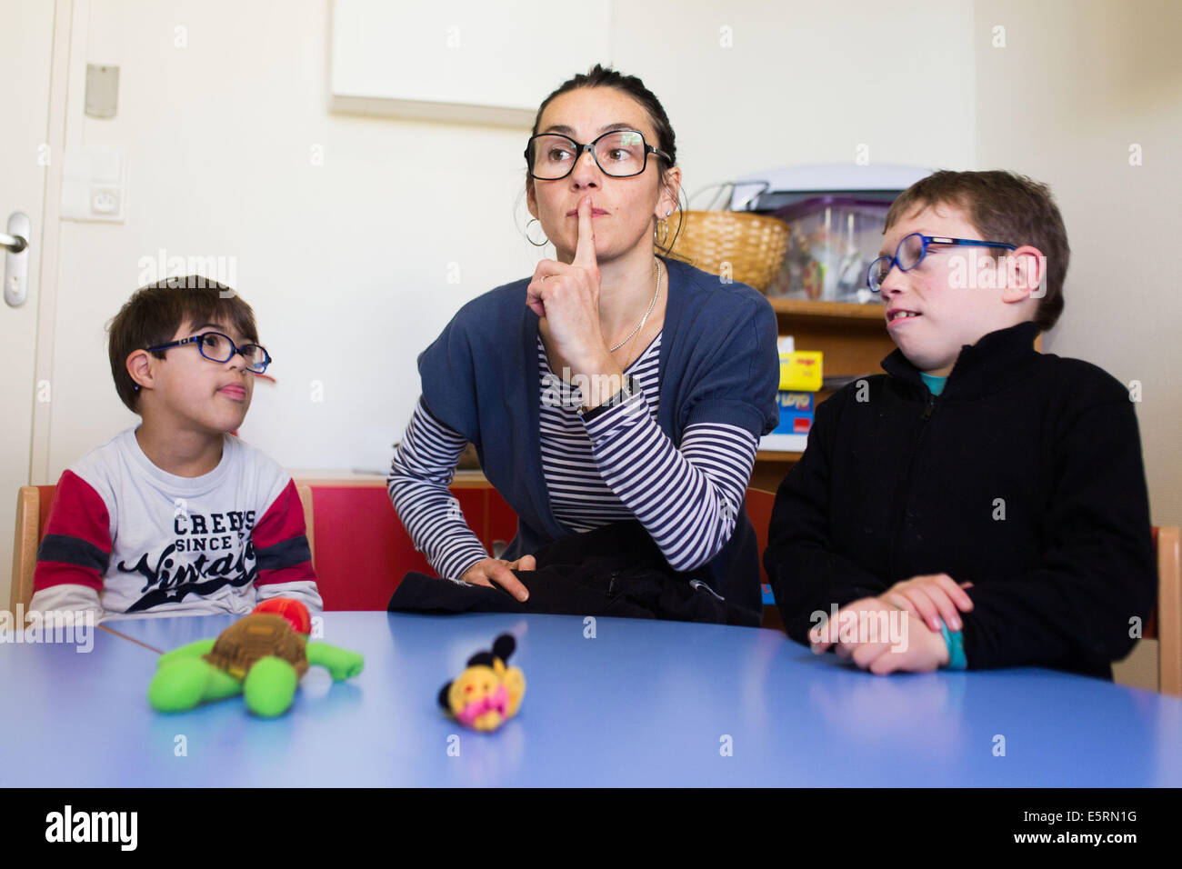 7 years old boys down's syndrome educated in an IME with Special education teacher teaching sign language. Medical-Educational Stock Photo