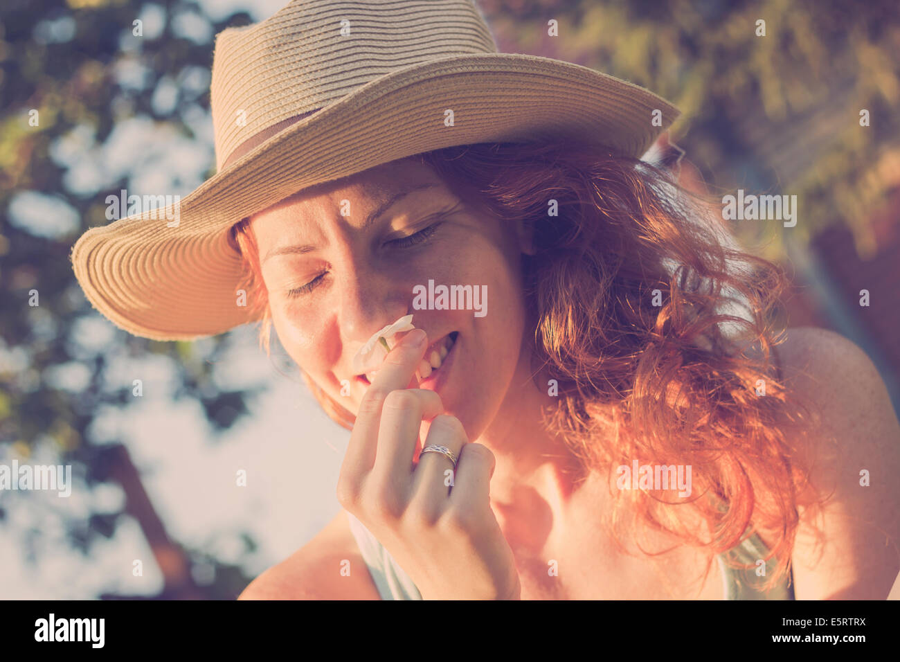 Beautiful girl with a hat smelling a flower, enjoying sunny summer day Stock Photo