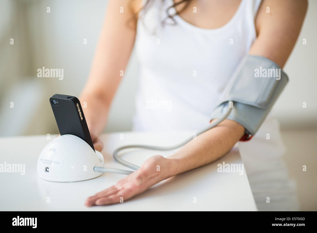 Woman taking her blood pressure with a docking station iPhone application iHealth®. Stock Photo