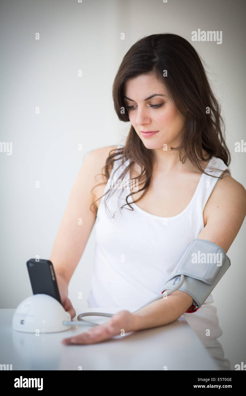 Woman taking her blood pressure with a docking station iPhone application iHealth®. Stock Photo
