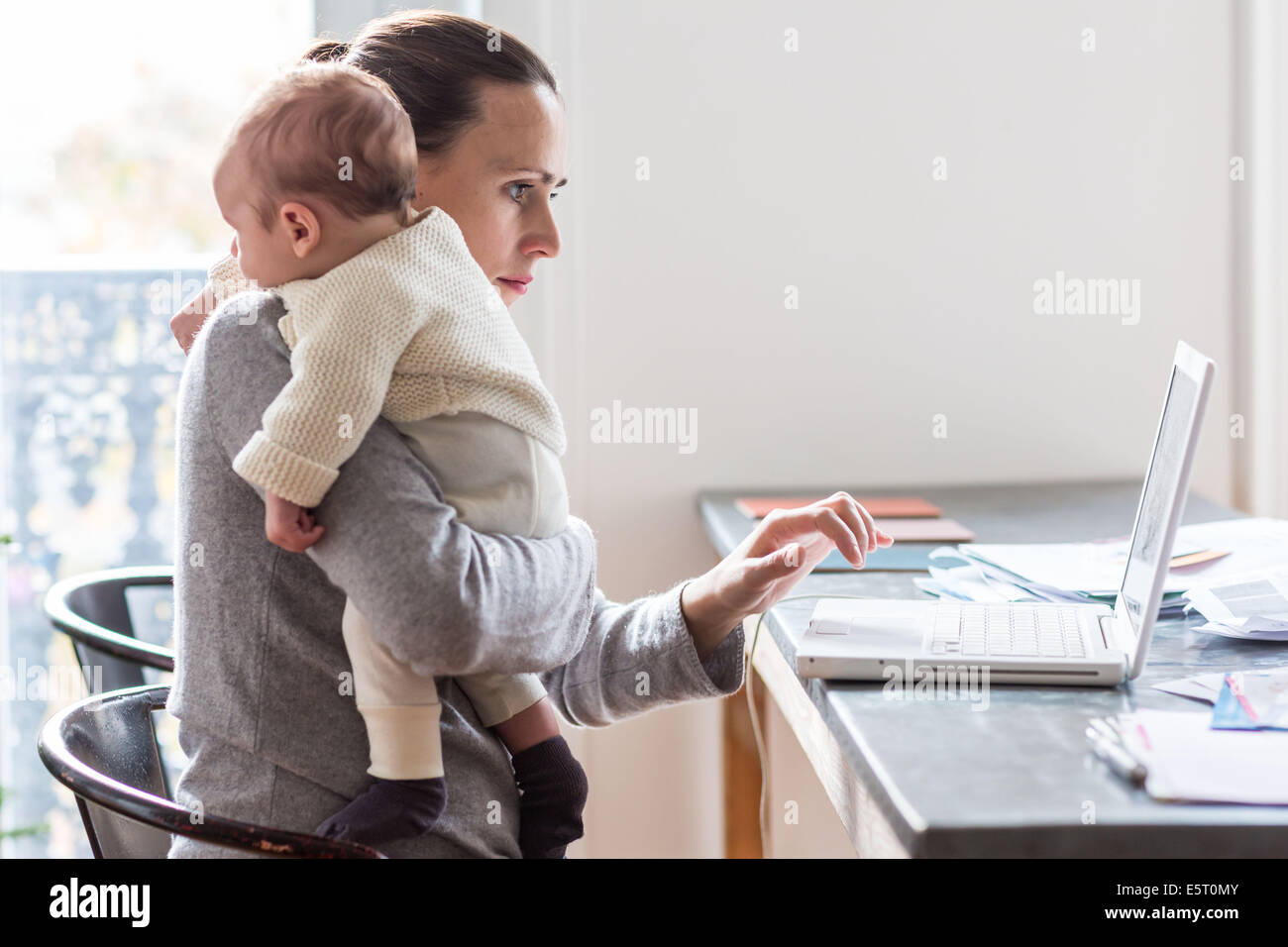 Woman using laptop computer with her 3 month old baby boy. Stock Photo