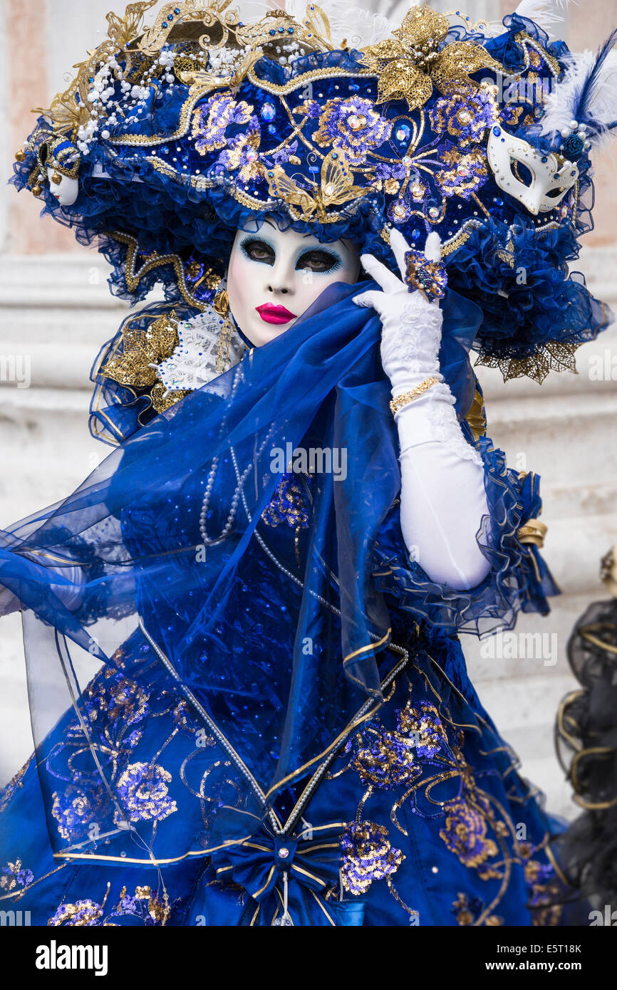 Woman in blue and gold costume with elaborate headdress in front of San Zaccaria Church during Carnival in Venice. Stock Photo