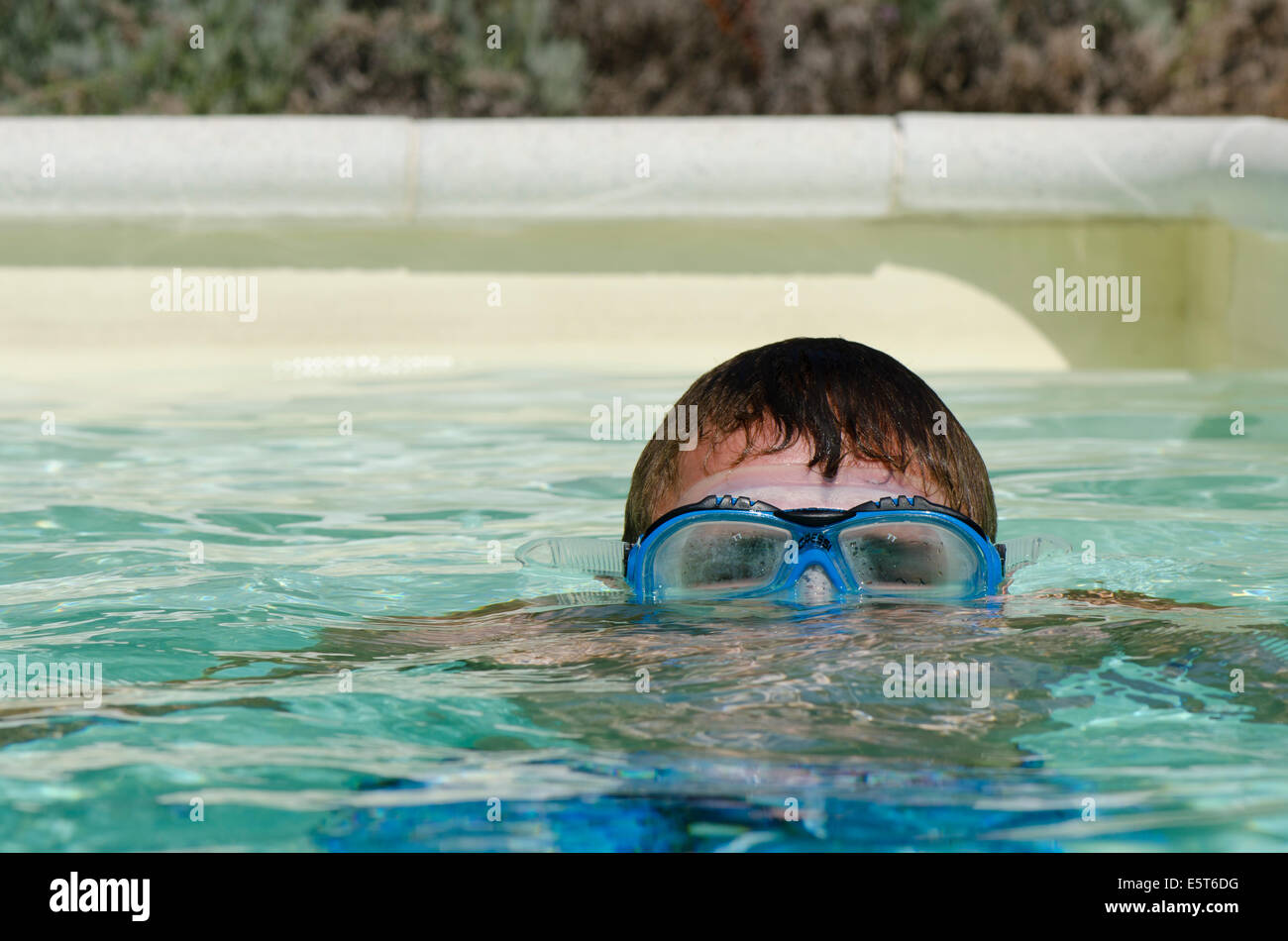 Teenager boy submerged wearing diving mask or goggles in swimming pool. Stock Photo