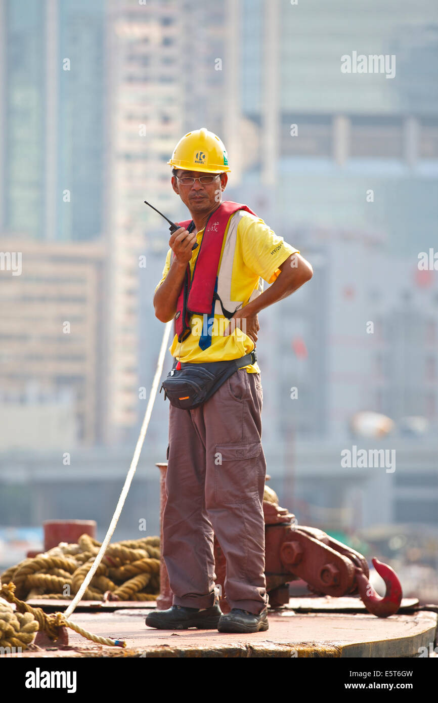 Asian Engineer Supervises The Dredging Of The Causeway Bay Typhoon Shelter, Hong Kong Cityscape Behind. Stock Photo