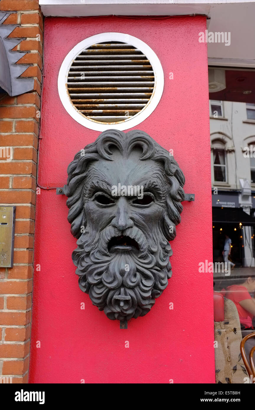 metal face sculpture of man with beard on red wall Stock Photo