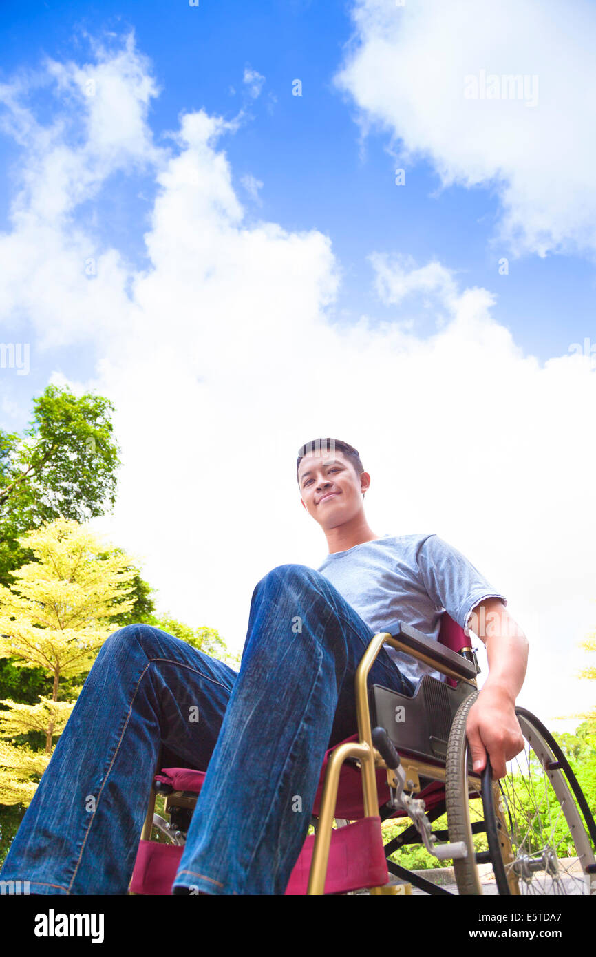smiling young man sitting on a wheelchair with natural background Stock Photo