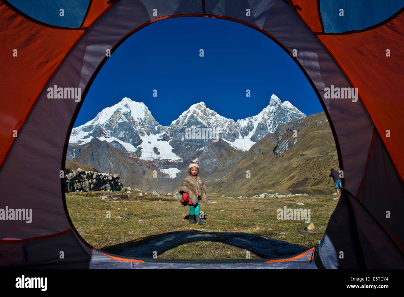 View of a local girl from a tent, at the back the snow-capped mountains from left Mt Yerupaja Grande, Mt Yerupaja Chico and Mt Stock Photo