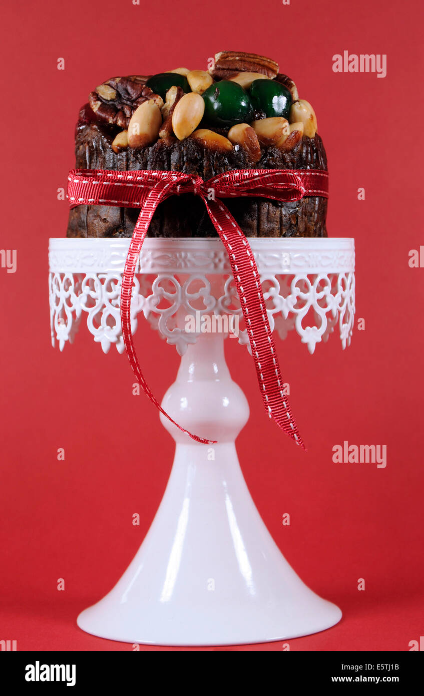 Festive Christmas food, fruit cake with glacé cherries and nuts on white cake against a red background. Stock Photo