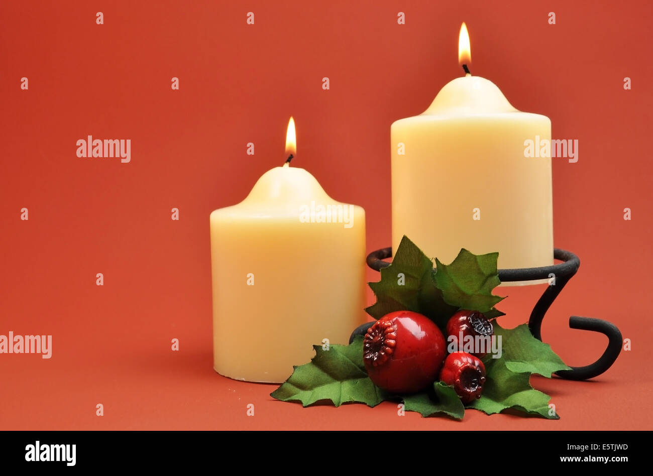 A pair of two creamy white lit candles with green and red holly ...
