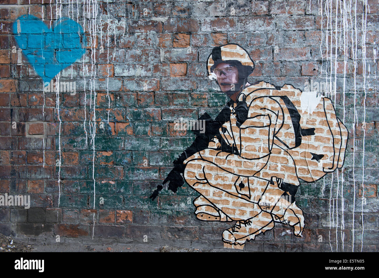 A streetart stencil of a military sniper crouching near a large blue heart. Stock Photo
