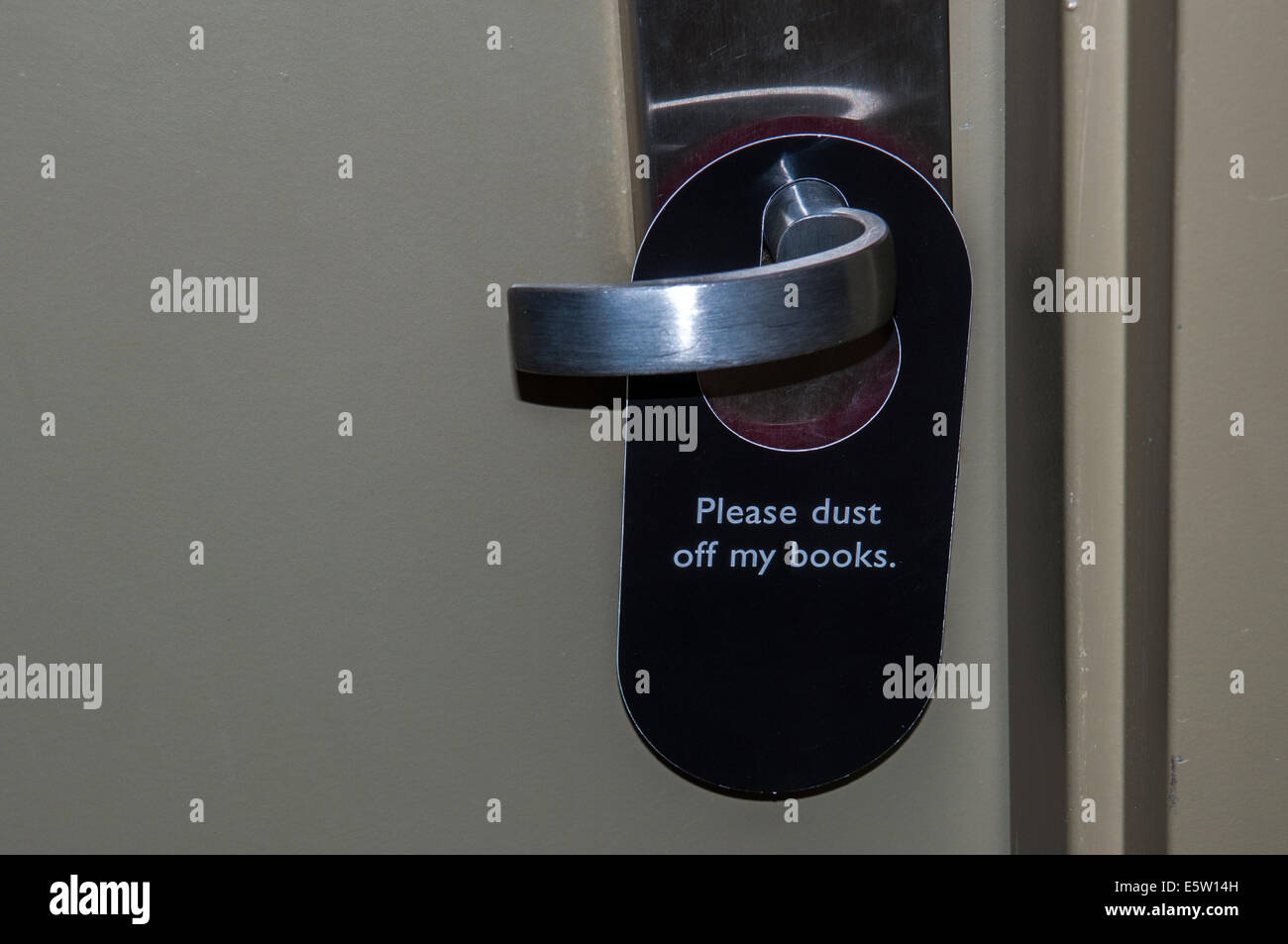 A 'Please dust of my books' sign hangs on a hotel room door handle indicating the room needs cleaning. Stock Photo