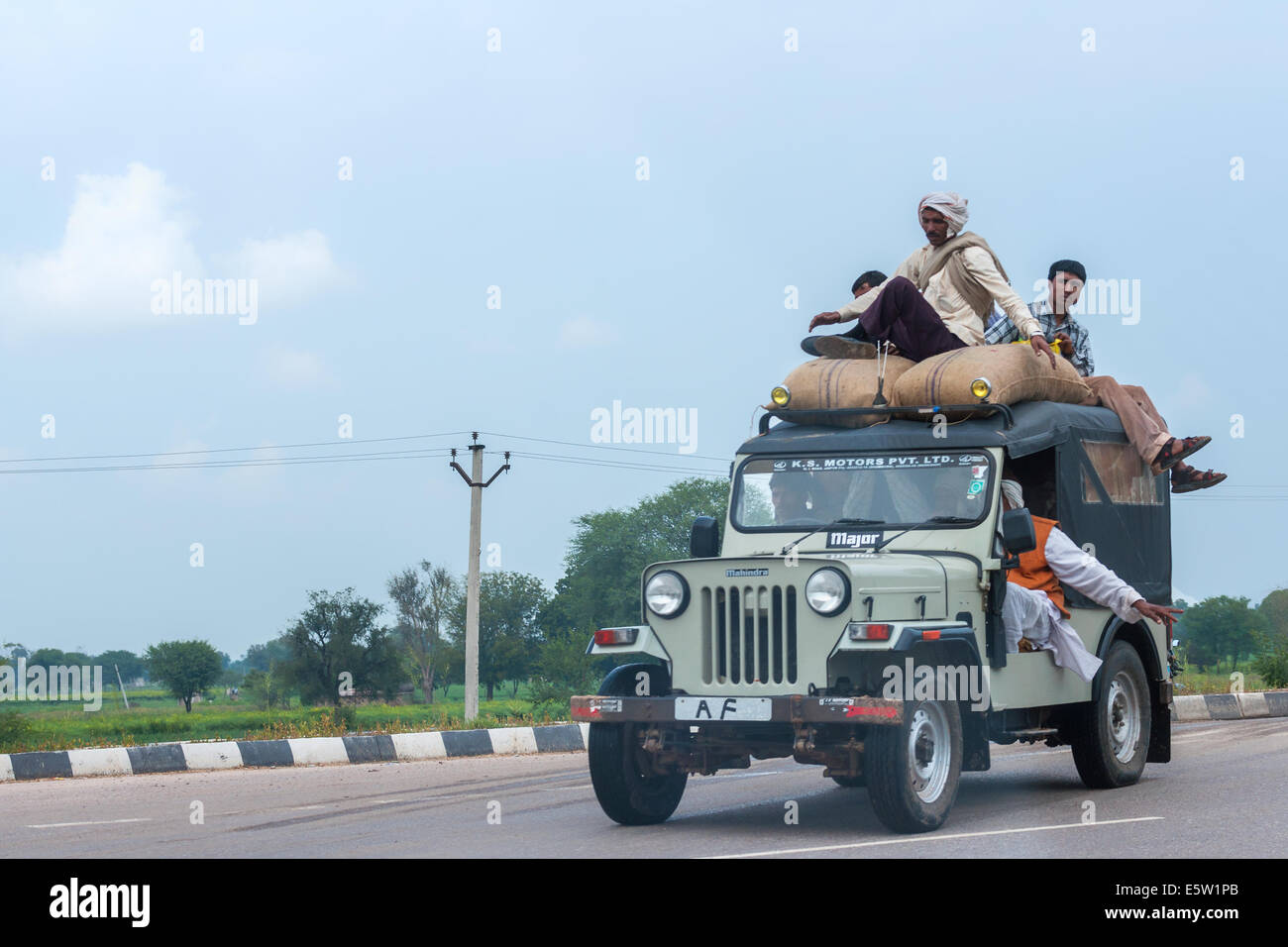Overloaded jeep with bags and people on the roof driving on the road. Stock Photo