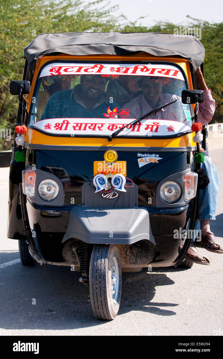 Happy faces inside the auto-rickshaw on this sunny day. The frontal view of the black-yellow car fills 80% of the picture. Stock Photo