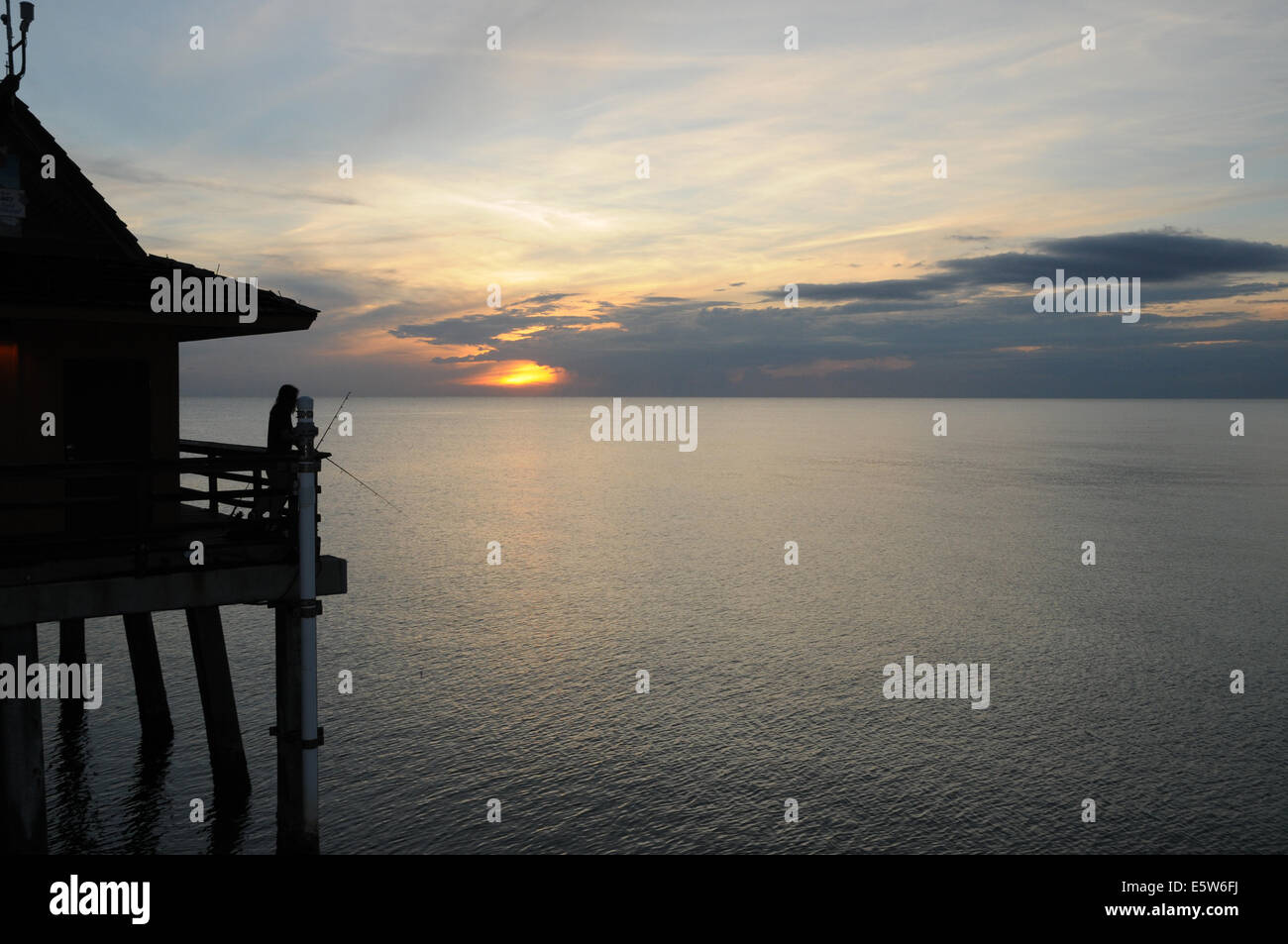 A lone fisherman tries his luck at sunset from Naples Pier, Florida Stock Photo