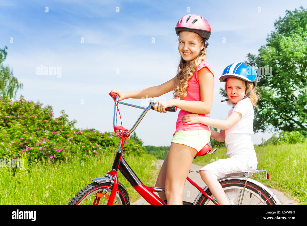 Two little girls sitting on a bicycle outdoors Stock Photo