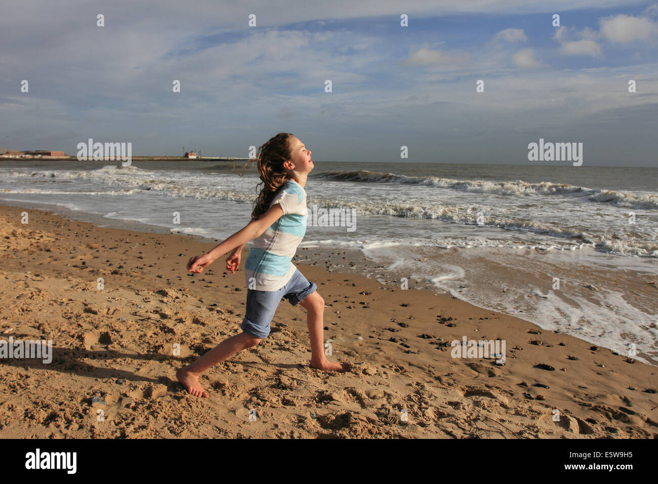 little girl running along sandy bach, east coast.Norfolk, UK Stock Photo