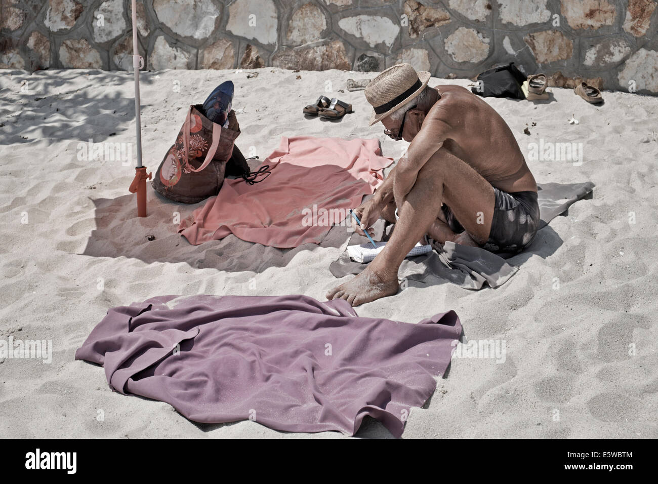 Man occupying his time on the beach by completing a word puzzle quiz. Stock Photo
