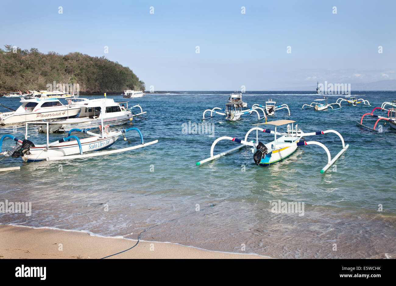 Fleet of traditional Indonesian Jukung fishing boats in Padangbai bay harbour, Bali. Beautiful clear blue sea with collection of boats floating Stock Photo