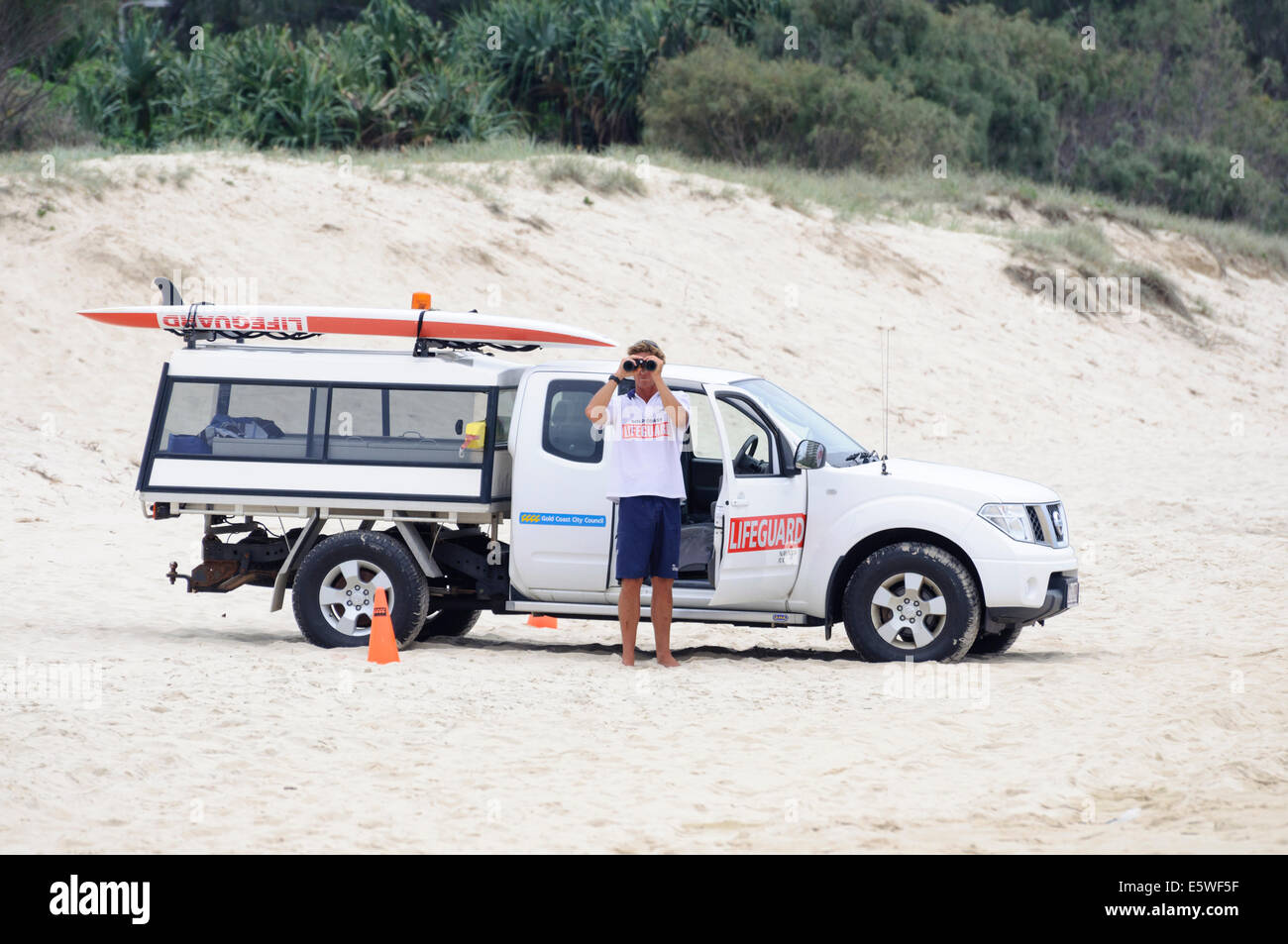 Lifeguard watches the beach while standing besides his specialised vehicle, ready to respond at a moment's notice. Stock Photo