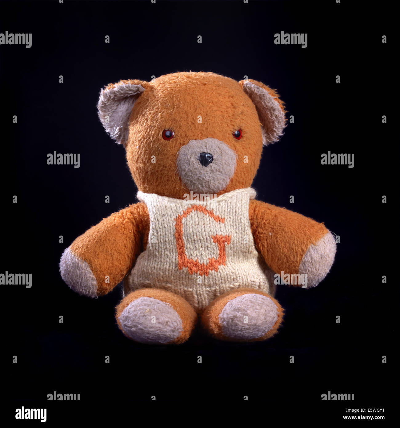 Studio shot of vintage worn large ginger orange bear with hand knitted  cream jumper embellished with the letter 'G' Stock Photo - Alamy