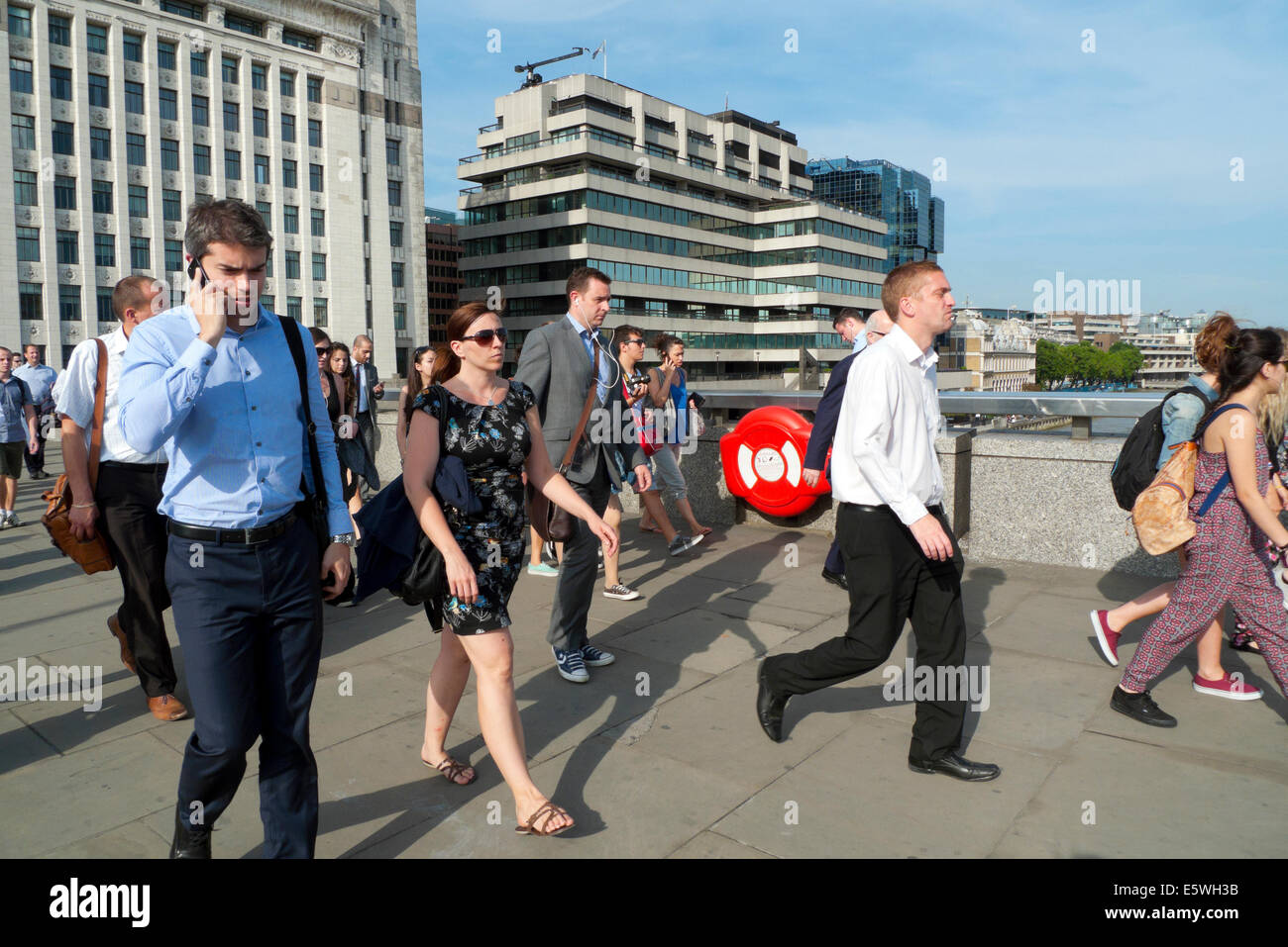 People walking across London Bridge at rush hour after work in summer & man talking on mobile cell phone London UK  KATHY DEWITT Stock Photo