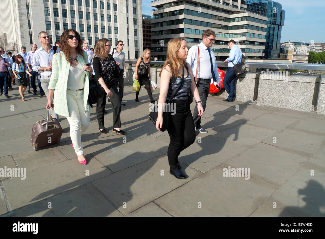 Woman with wheeled luggage and people walking across London Bridge over River thames at rush