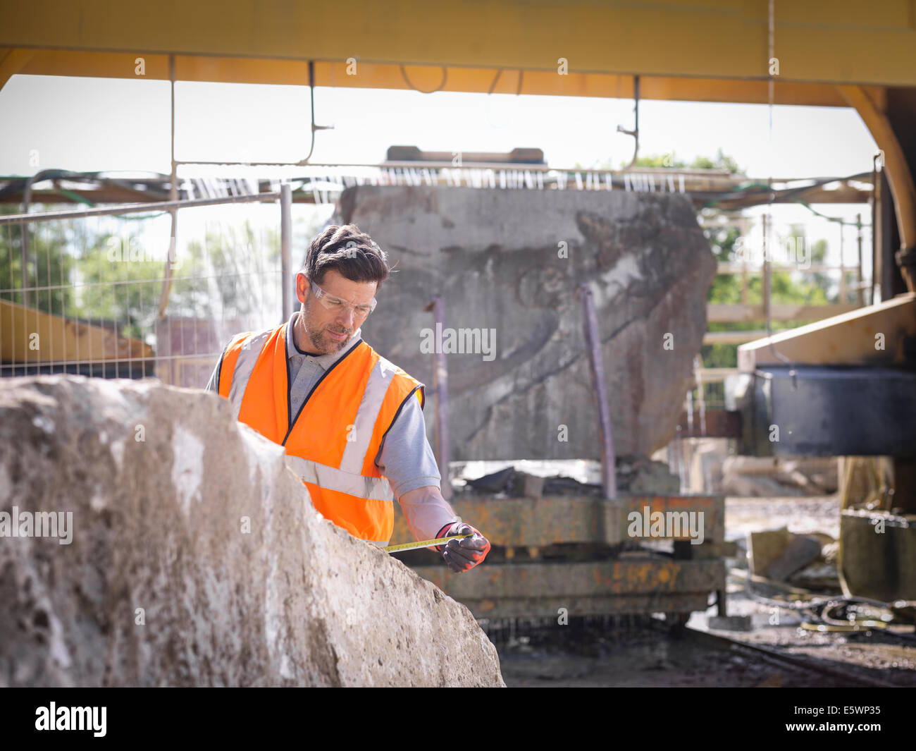 Quarry worker measuring rock in front of stone saw Stock Photo