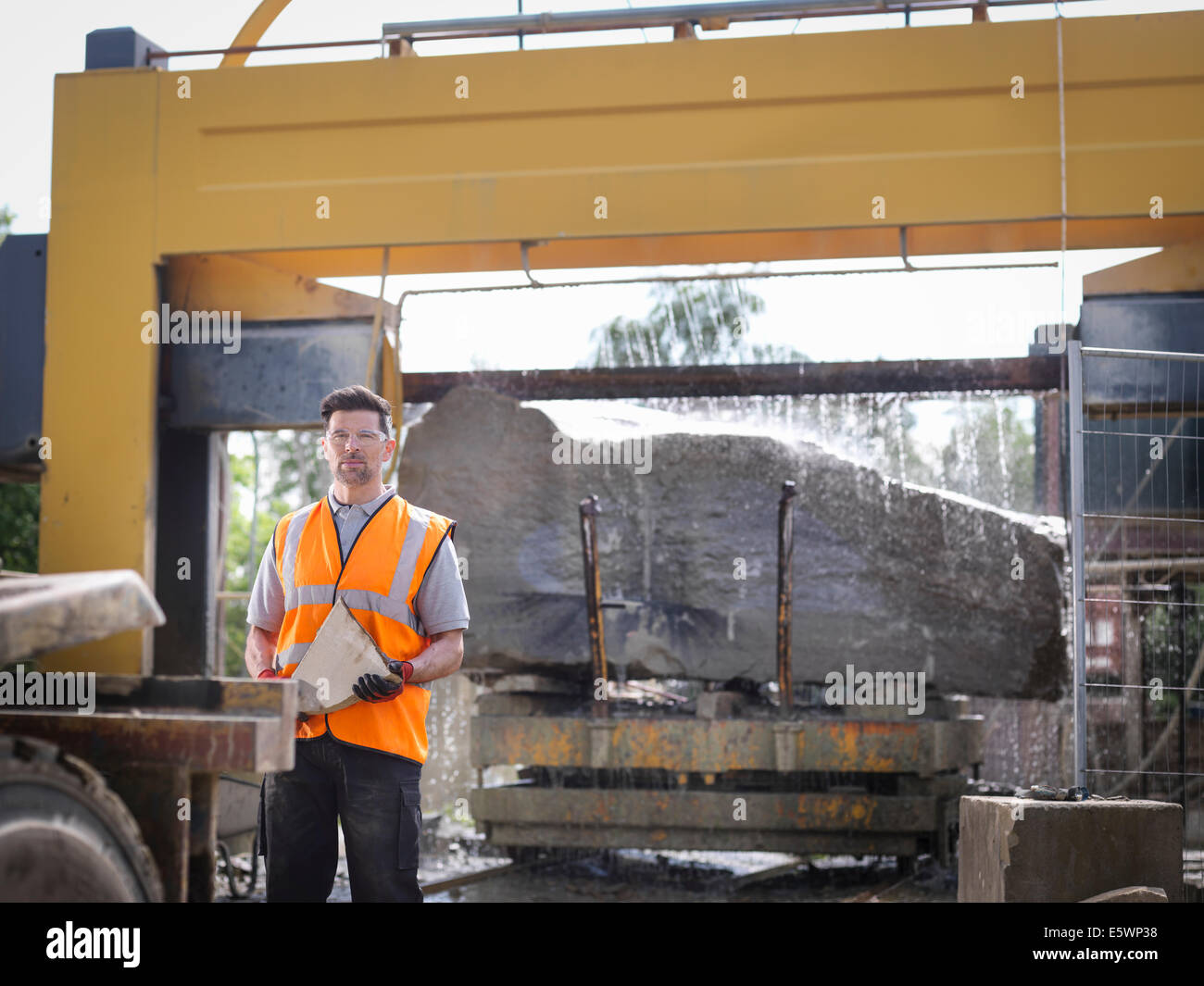 Portrait of quarry worker in front of large rock being cut in stone saw Stock Photo