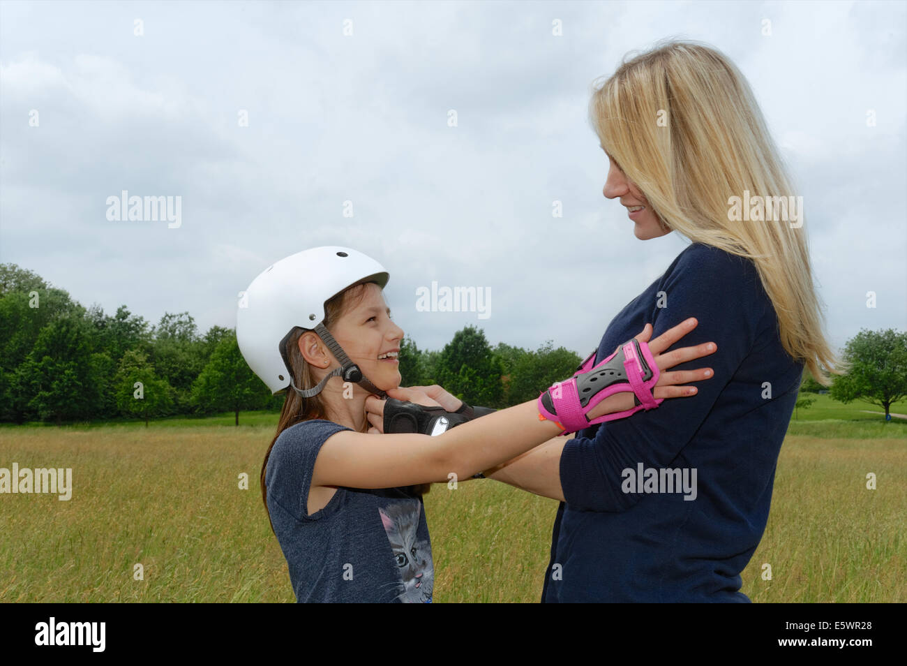 Mother fastening daughter's rollerblading helmet in park Stock Photo