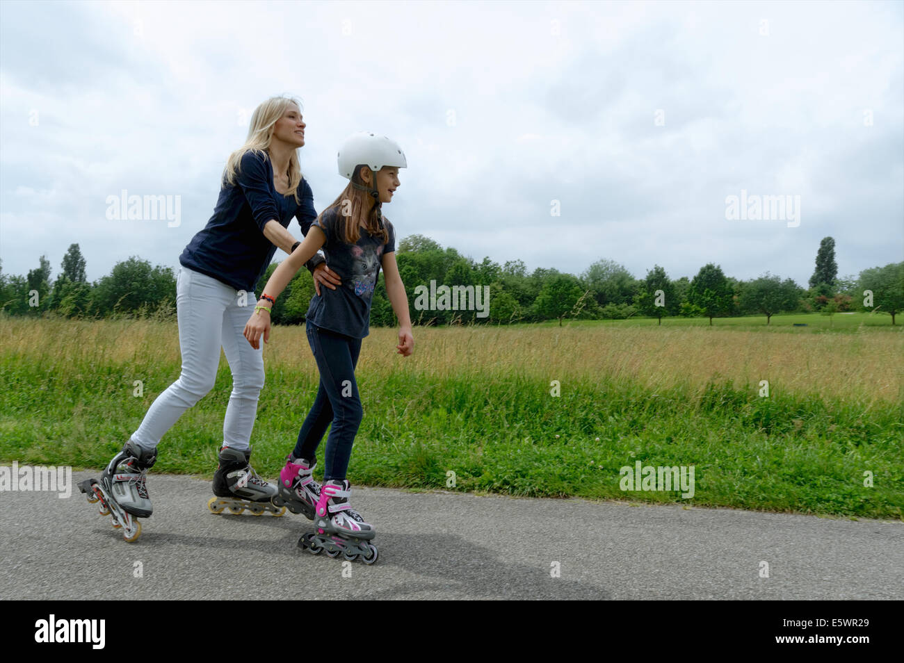 Mother holding onto daughter whilst rollerblading in park Stock Photo