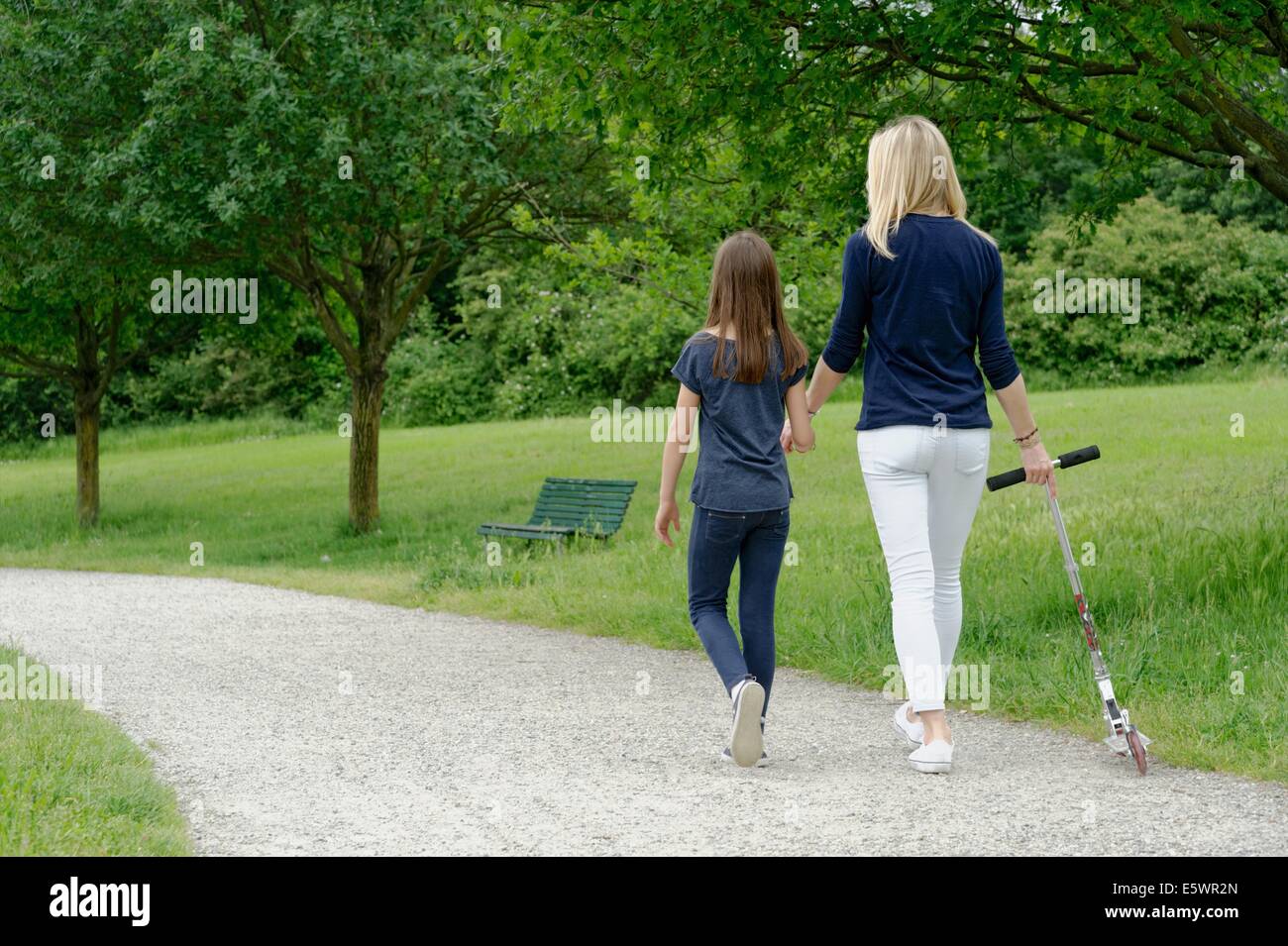 Mother and daughter strolling in park with scooter Stock Photo