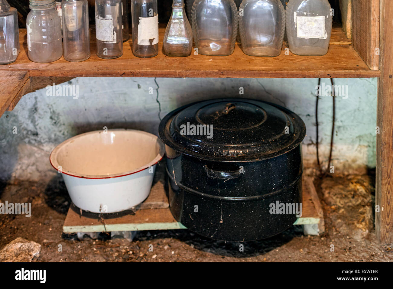Old enameled steel pot with lid, pan and bottles on wooden pantry