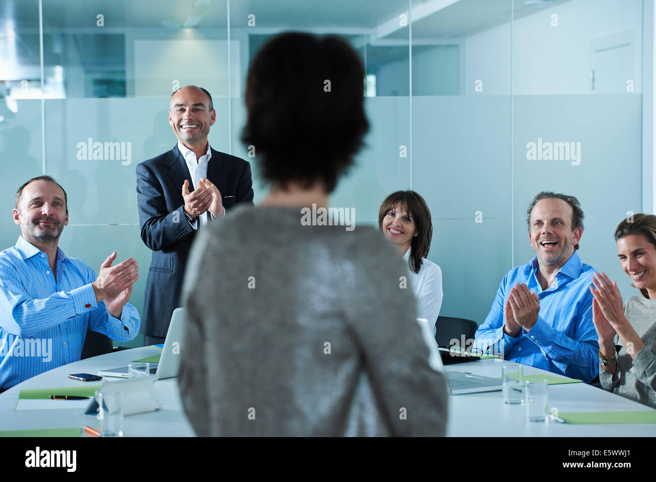 Businessmen and women applauding around boardroom table Stock Photo
