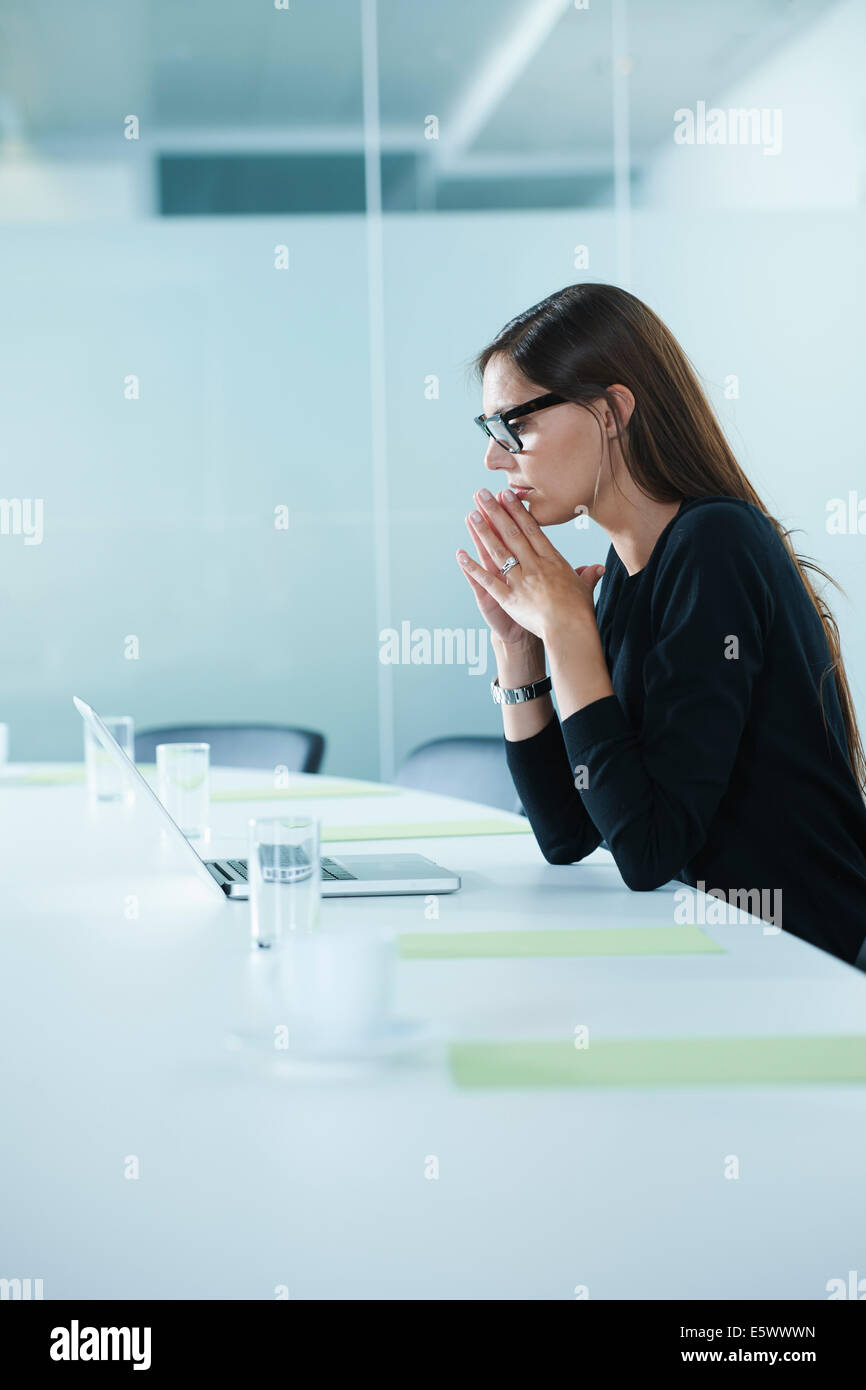 Worried female office worker using laptop at conference table Stock Photo