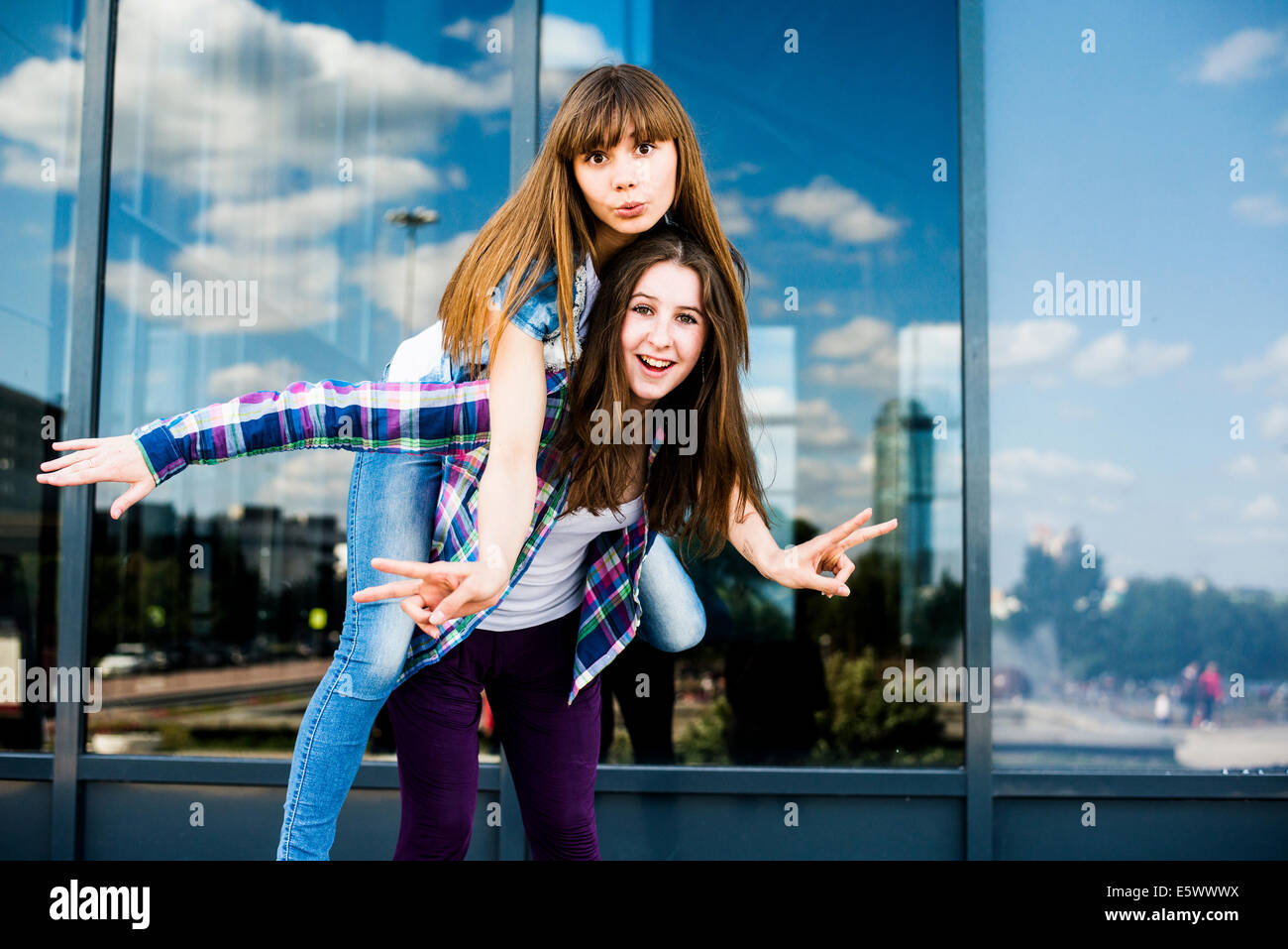 Two young women piggybacking and making peace signs Stock Photo