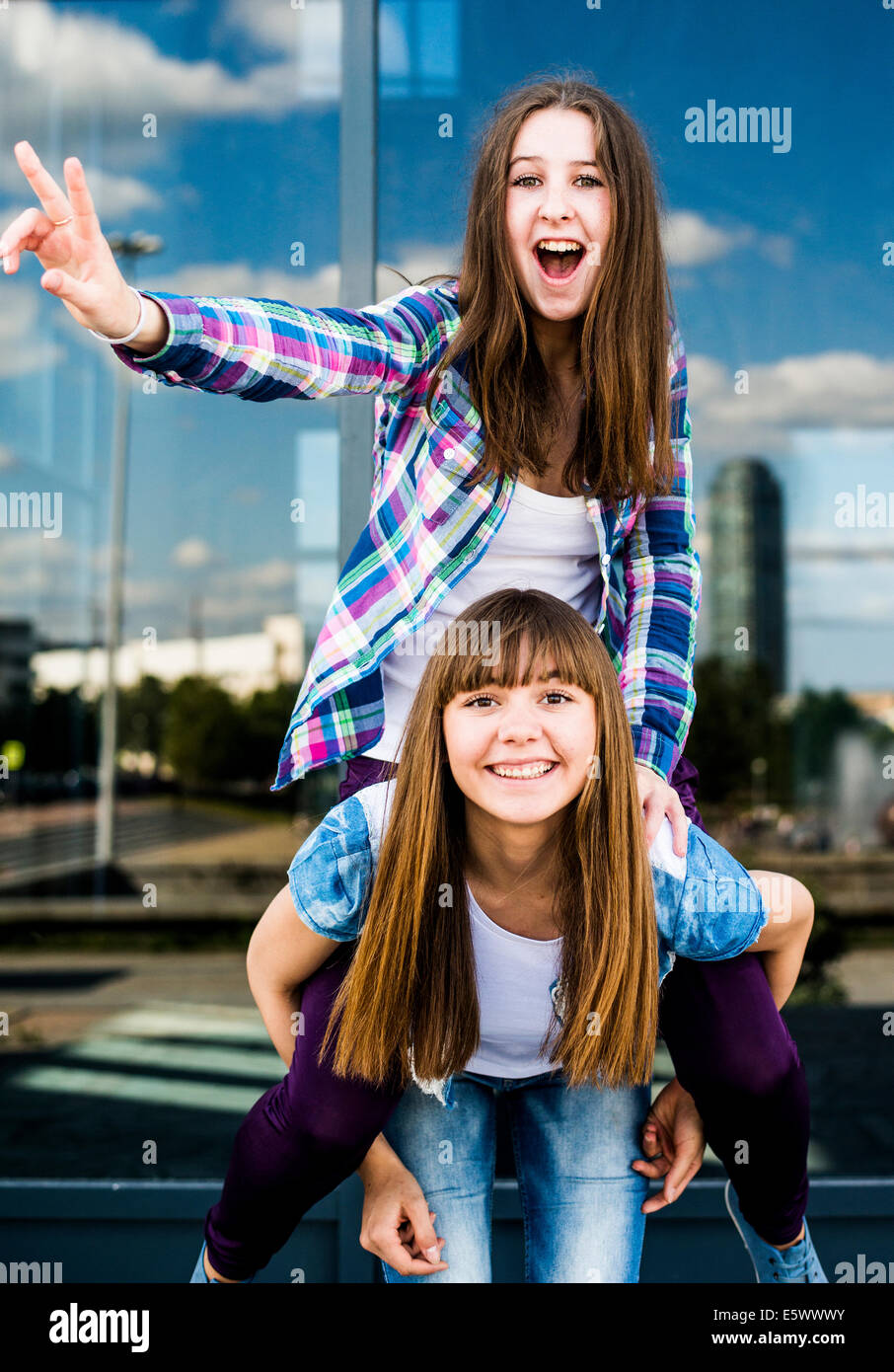 Two young women making peace signs and piggybacking Stock Photo