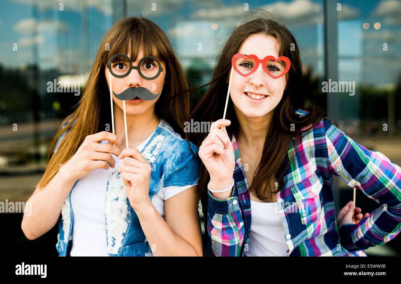 Portrait of two young women holding up mustache and eyeglass costume masks Stock Photo