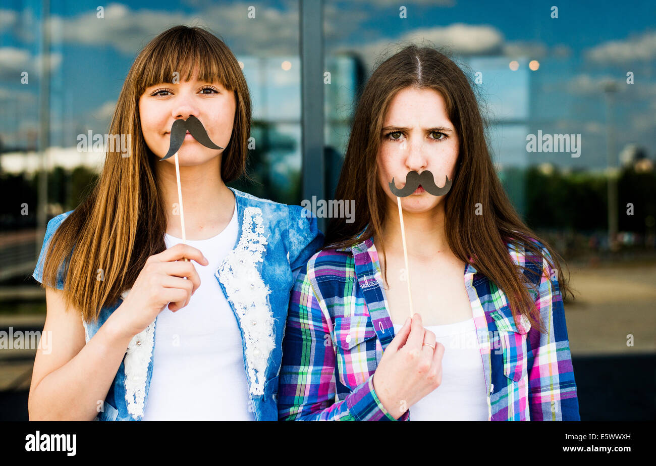 Portrait of two young women holding up mustache costume masks Stock Photo
