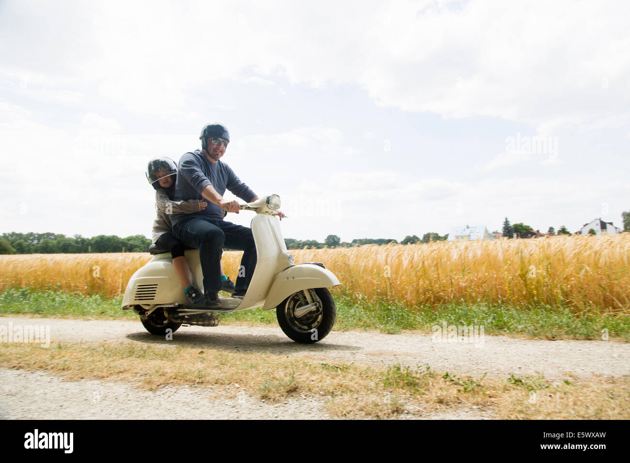 Mature man and daughter riding motor scooter along dirt track Stock Photo