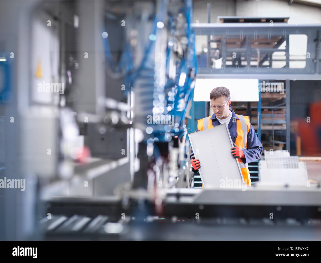 Worker inspecting parts next to robotic metal cutting machine in sheet metal factory Stock Photo