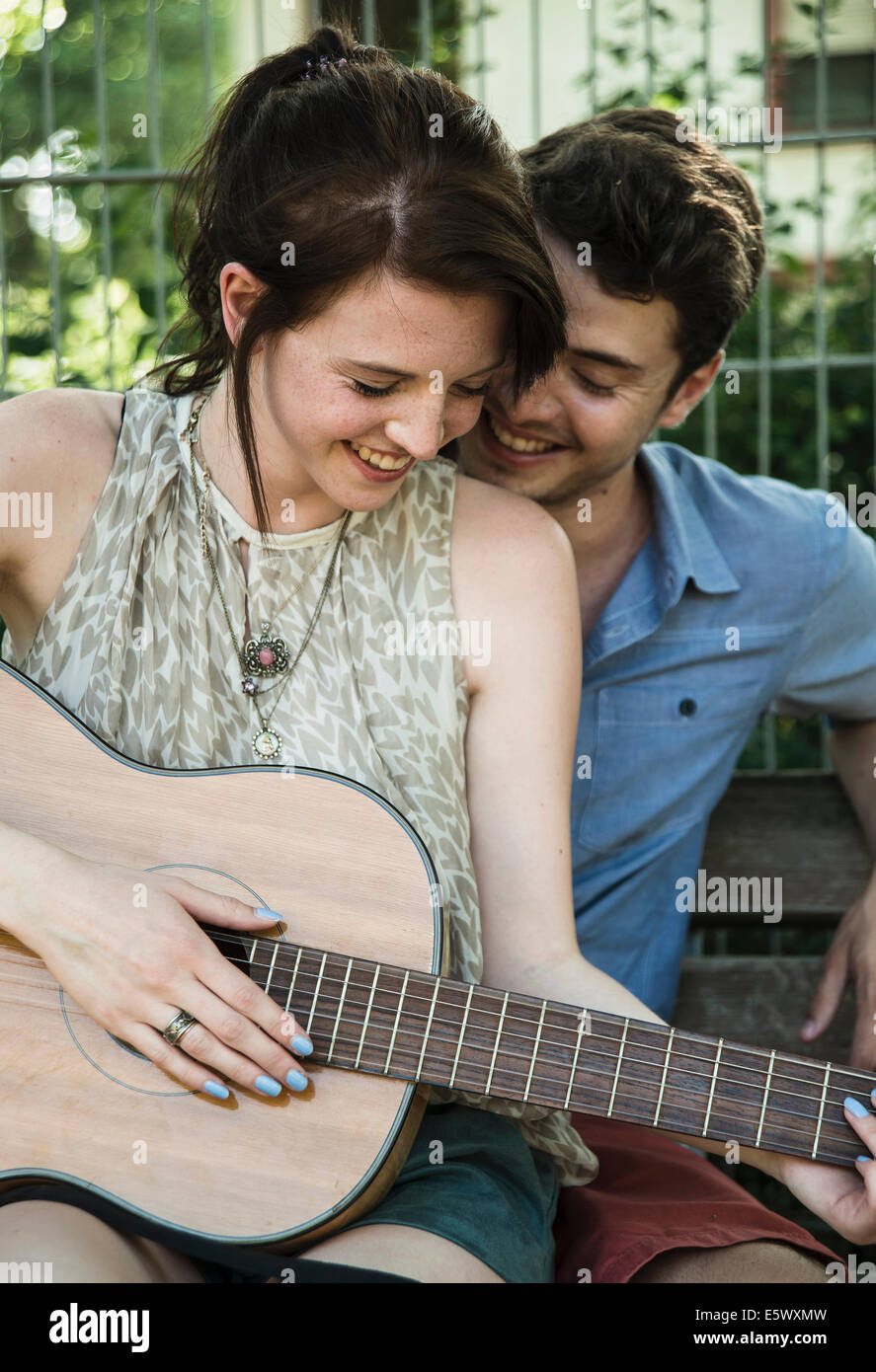 Young couple serenading on acoustic guitar in park Stock Photo