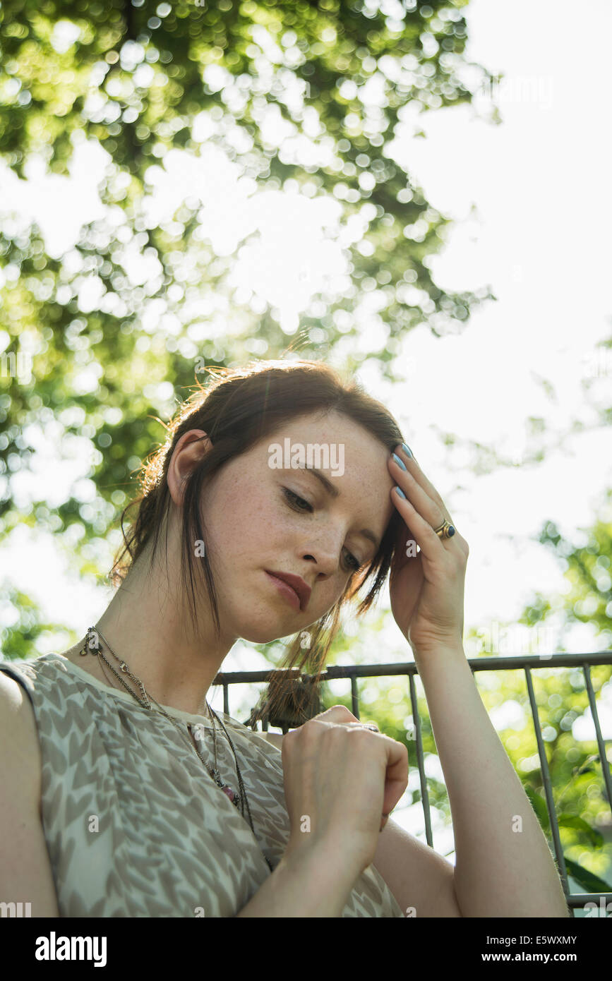 Portrait of sullen young woman with hand on her head in park Stock Photo