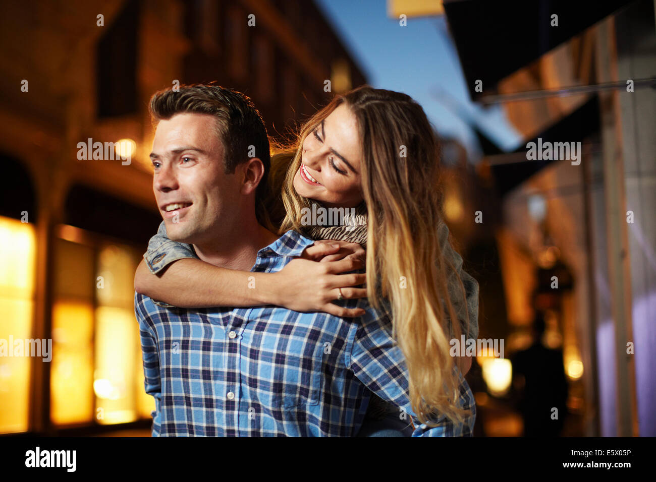 Couple giving piggy back on city street at night Stock Photo