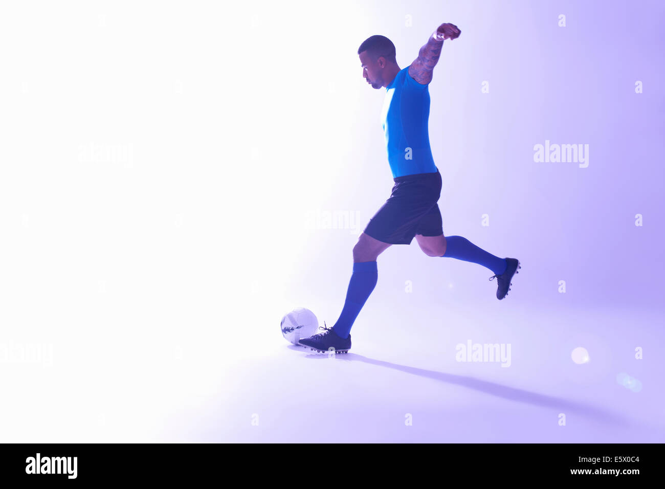 Studio shot of young male soccer player with arms outstretched kicking the ball Stock Photo