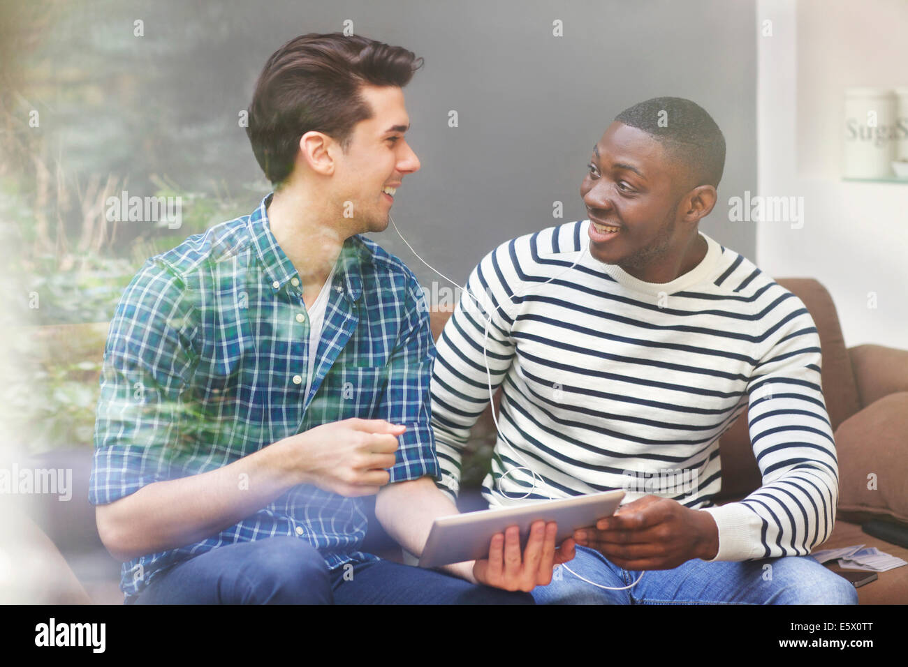 Two young male friends listening to music on digital tablet behind window Stock Photo