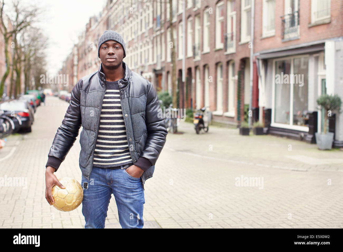 Portrait of young man on street holding soccer ball, Amsterdam, Netherlands Stock Photo